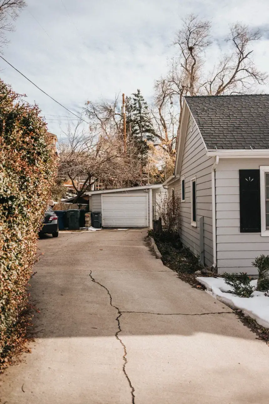 Long concrete drive beside white siding, the surface dulled by weather
