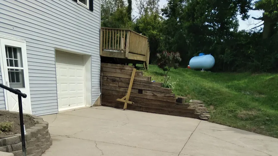 Washed lap siding and a clean concrete drive beside a timber retaining wall