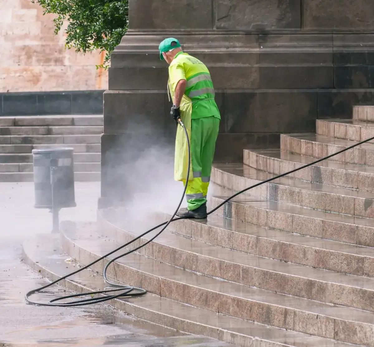 Worker pressure washing a flight of stone steps, spray and mist rising off the treads